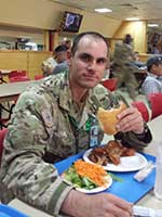 Photo: Boris in his army gear, eating a hamburger with plates of meat and vegetables in front of him.